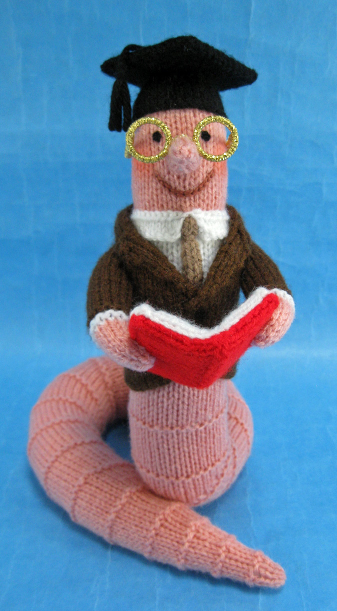 A knitted toy of a scholarly looking worm reading a book